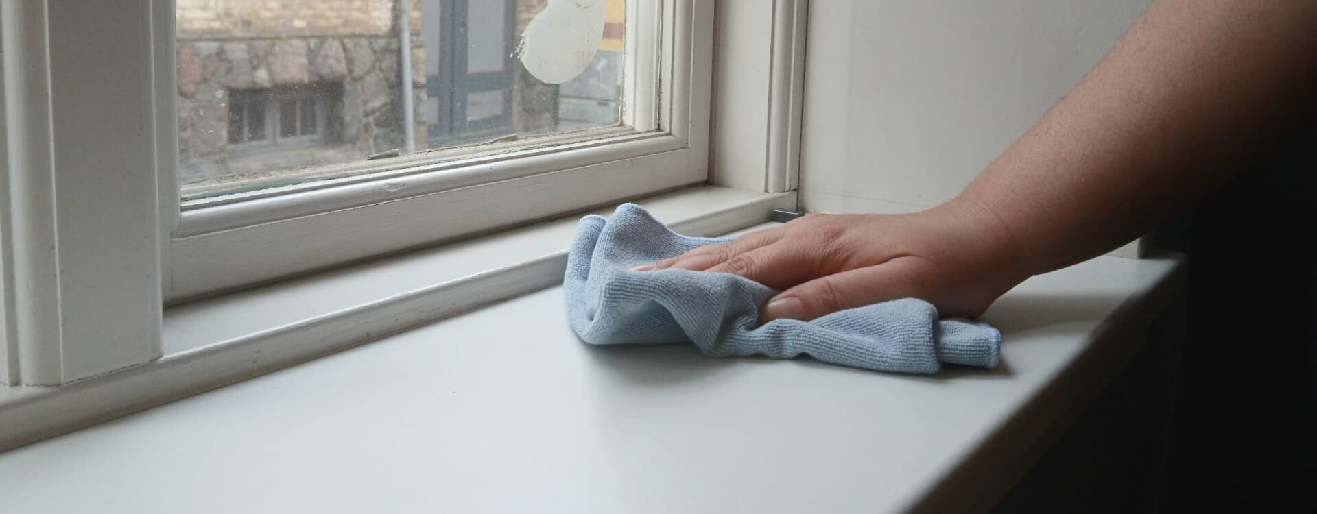 Hånd der aftørrer vindueskarm med mikrofiberklud – erhvervsrengøring i faaborg